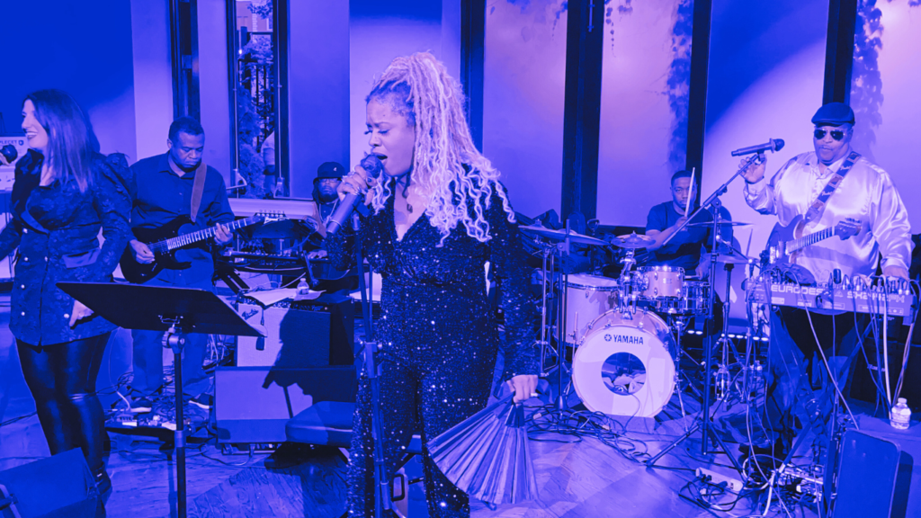 Two female vocalists singing side by side with live band backing them at a nighttime event